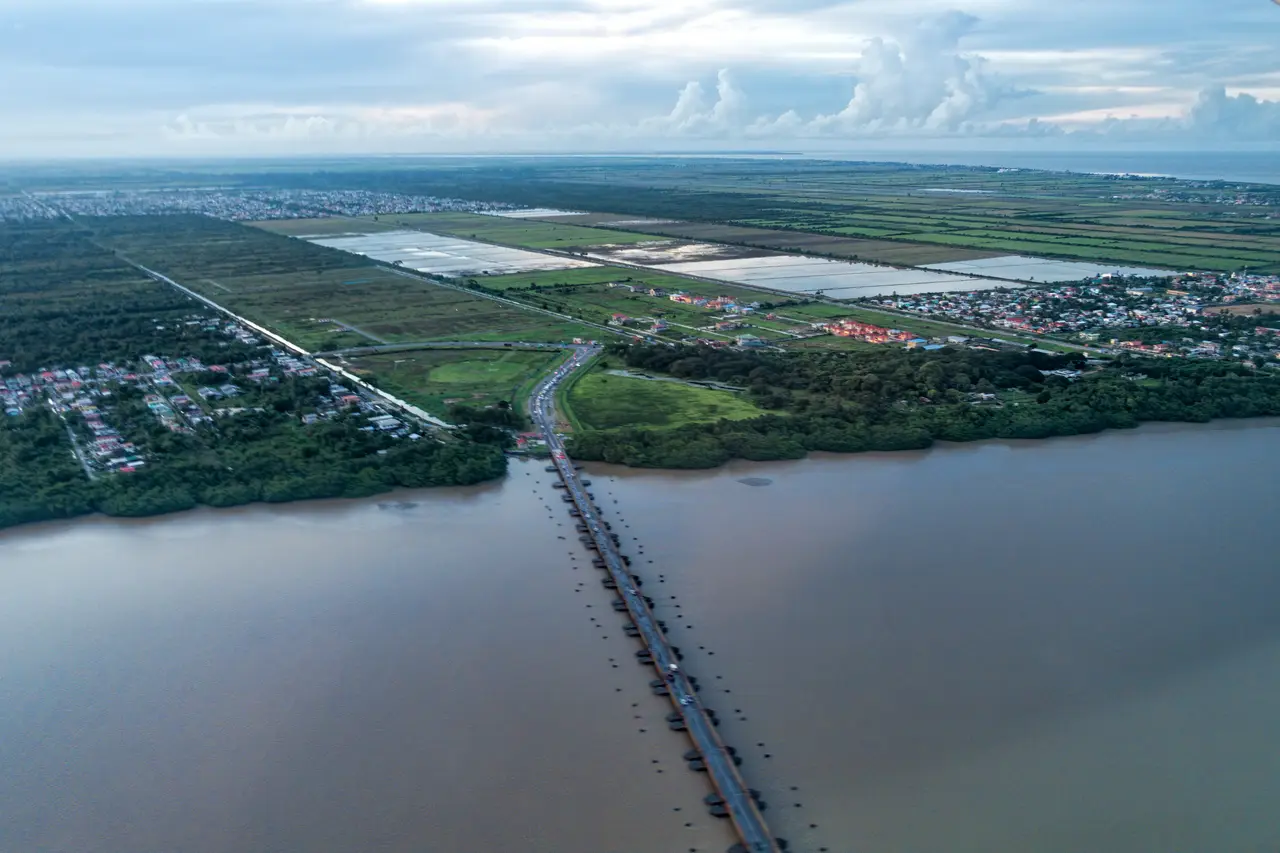 The long, low floating Demerara Harbour Bridge running across the wide Demerara River towards flat coastal land and roads