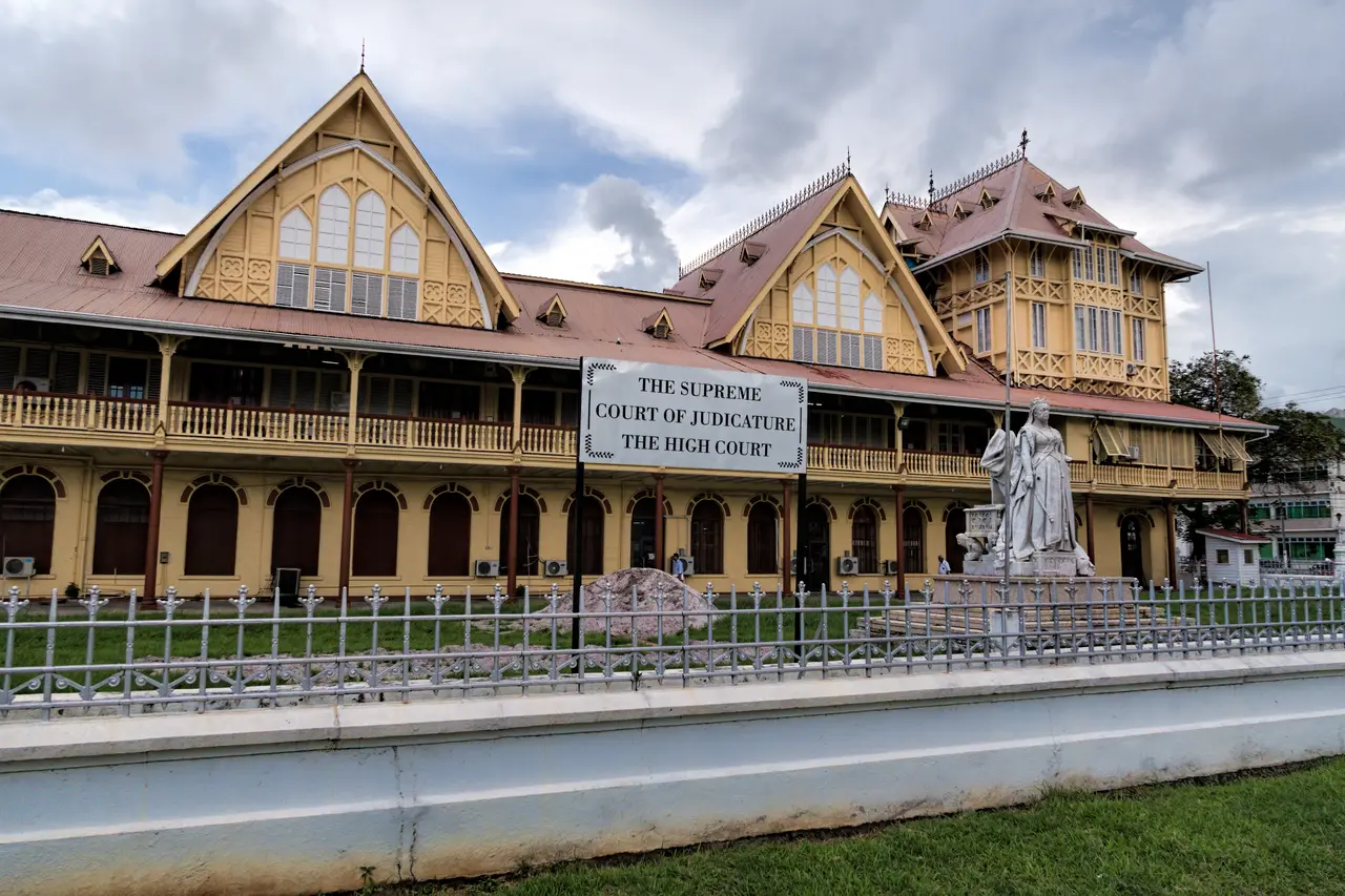 The ornate 1887 timber-framed High Court building in Georgetown with a statue in front and a sign reading The Supreme Court of Judicature