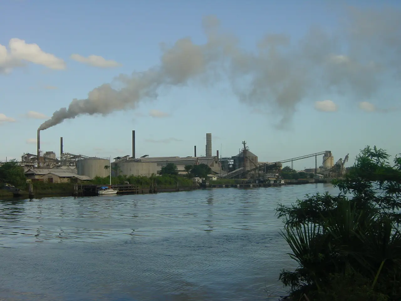 Industrial buildings and a smoking chimney of the Linden bauxite plant on the far bank of the Demerara River