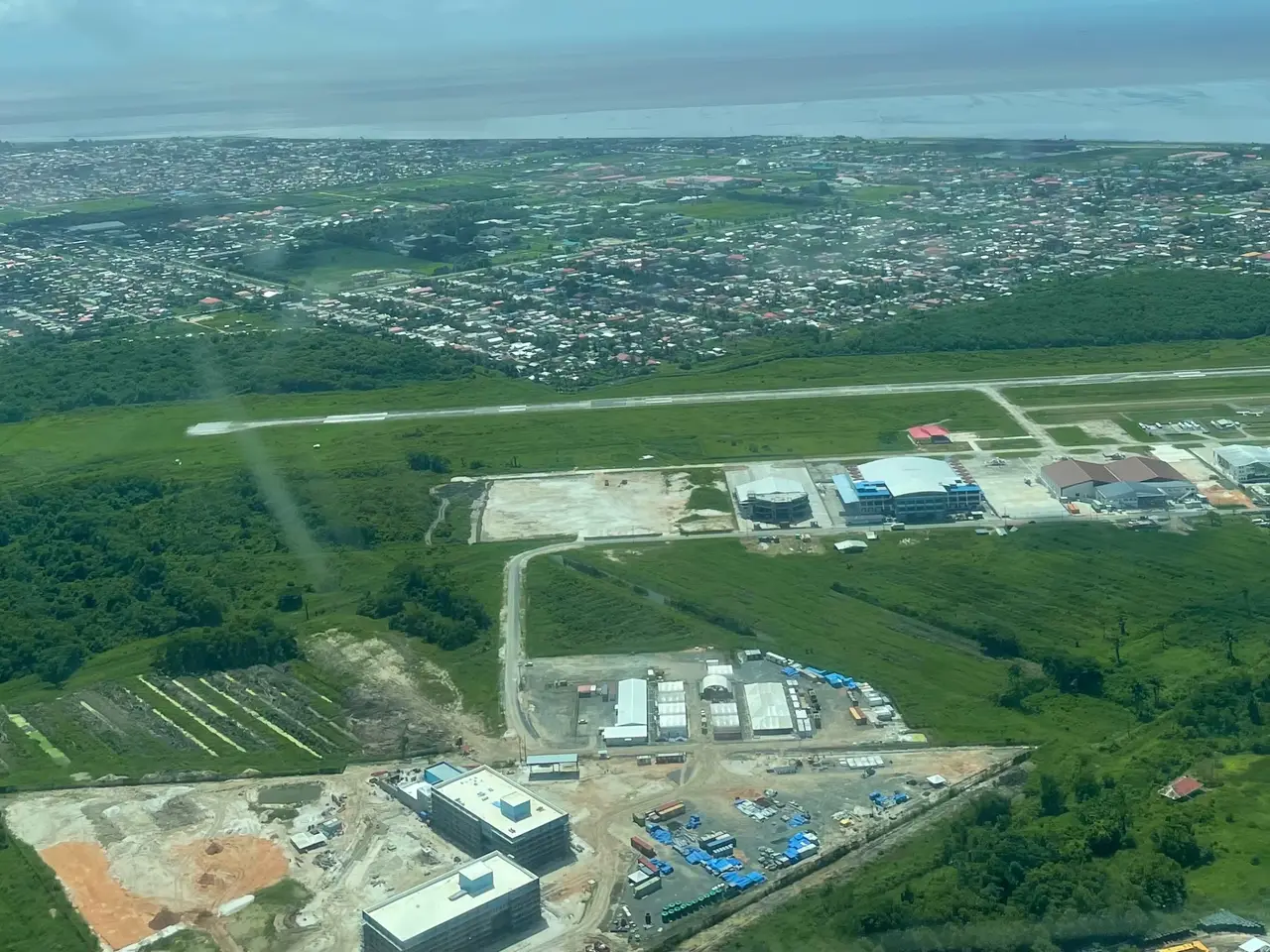 Aerial view of a runway and terminal buildings among green land on the coast, with the suburbs of Georgetown beyond