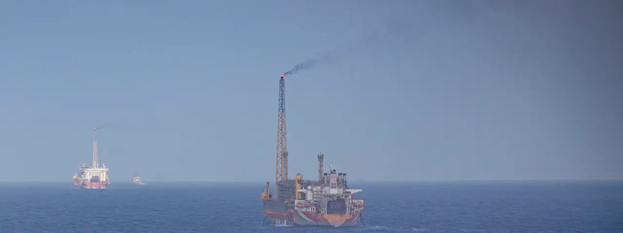 An FPSO production vessel with a tall flare tower on the open Atlantic, with a second production vessel and a support ship on the horizon