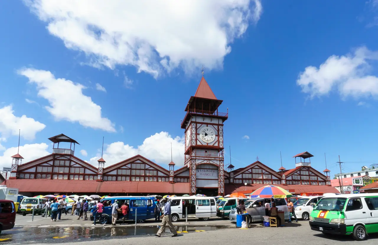 Stabroek Market's iron clock tower and long market hall, with minibuses and traders' umbrellas in front